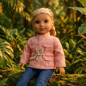 May include: A doll with blonde hair in a braid, wearing a pink jacket with four pockets and blue jeans. The doll is sitting on a moss-covered log, surrounded by lush green foliage.