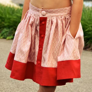 May include: A red and pink skirt with a button-up front and a white and pink floral pattern. The skirt has a gathered waist and a flared silhouette.