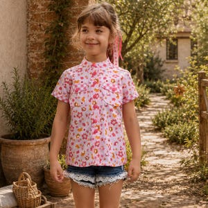 May include: A short-sleeved button-down shirt featuring a pink and white floral pattern with a small gingham check detail on the chest pockets, paired with dark blue denim shorts that have a white lace trim along the bottom hem edges.