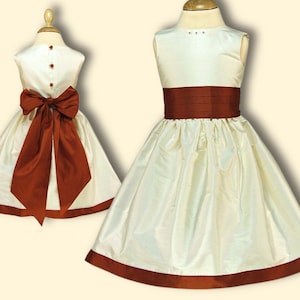 May include: A white sleeveless dress with a rust-colored sash and trim. The dress has a full skirt and a bow in the back.