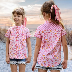 May include: A pink and white short-sleeved button-up shirt with a floral print and gingham pattern. The shirt has a mandarin collar and two patch pockets.
