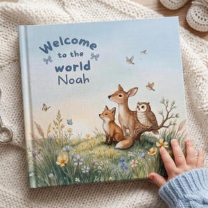 Peut inclure: Un livre à couverture rigide carré avec une couverture bleu clair portant le texte Welcome to the world Noah. L'illustration représente un cerf, un renard et un hibou assis dans une prairie herbeuse remplie de fleurs sauvages, de papillons et d'oiseaux.