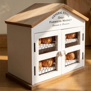 May include: A white wooden egg storage cabinet shaped like a house with a natural wood roof. The front features two doors with wire mesh panels and round white knobs. Text on the front reads GENERAL STORE Vintage FARMERS MARKET Groceries & Provisions.