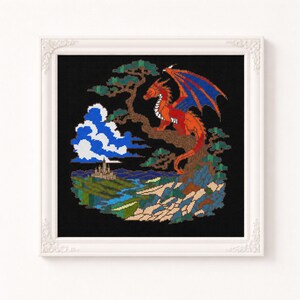 May include: A framed cross-stitch embroidery featuring a red dragon with blue-accented wings perched on a brown tree. The scene includes a white cloud, a distant castle, a blue river, and green landscape elements set against a solid black background.