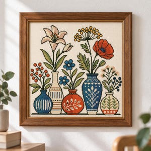 May include: A framed cross-stitch embroidery featuring five distinct vases holding various colorful flowers, including a lily, a poppy, and small blue and orange blossoms, all set against a cream-colored fabric background within a dark wood frame.
