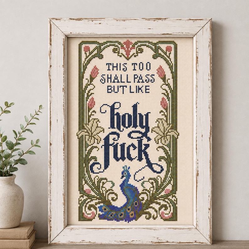 May include: A framed cross-stitch embroidery on cream fabric featuring a decorative green and pink floral border with a peacock at the bottom. The text reads: THIS TOO SHALL PASS BUT LIKE holy fuck, rendered in black and dark blue lettering.