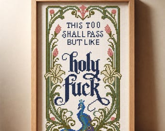 May include: A framed cross-stitch embroidery featuring a peacock at the bottom and floral borders in green and pink. The text reads: This too shall pass but like holy fuck. The design is set against a white fabric background within a light wood frame.