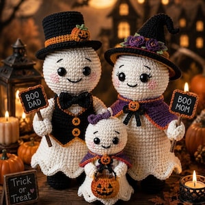 May include: Three crocheted ghost figures. The largest ghost wears a black top hat with a pumpkin and a black vest with a bow tie, holding a sign reading BOO DAD. The second ghost wears a witch hat with purple flowers, holding a sign reading BOO MOM. The smallest ghost wears a purple cape and holds a pumpkin bucket. A small sign reads Trick or Treat.