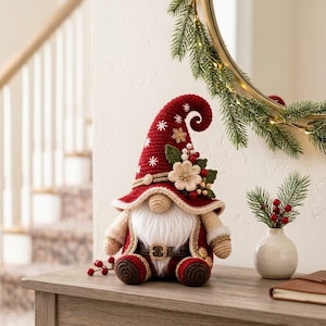 May include: A handcrafted crochet gnome figurine featuring a tall, pointed dark red hat adorned with white snowflake embroidery, a gold snowflake accent, a cream-colored flower, green leaves, and red berries. The gnome has a white beard and a belt.