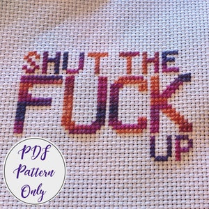 May include: A cross-stitch pattern featuring the phrase "Shut the Fuck Up" in a gradient of orange, red, and purple thread. The pattern is on white Aida cloth and includes a label that says "PDF Pattern Only".