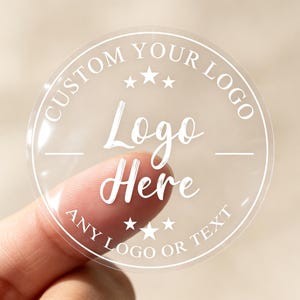 Peut inclure: Un autocollant circulaire transparent avec du texte imprimé blanc indiquant CUSTOM YOUR LOGO en haut, Logo Here au centre et ANY LOGO OR TEXT en bas, agrémenté de petites étoiles blanches au-dessus et au-dessous du texte central.