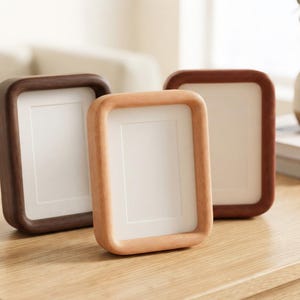 May include: Three rectangular picture frames with rounded corners, each featuring a smooth wooden finish in varying shades of light, medium, and dark brown. Each frame contains a plain white mat board insert, providing a clean display area.