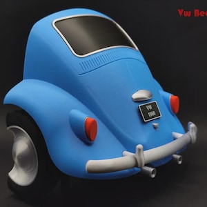 Puede incluir: Un coche modelo VW Beetle azul con ventana trasera negra, parachoques plateado y luces traseras rojas. El vehículo tiene una matrícula negra con el texto VW 1960. El texto Vw Beetle es visible en la esquina superior derecha de la imagen.