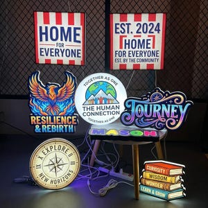 Peut inclure: Une collection d'enseignes lumineuses présentant divers motifs, dont un phénix avec le texte Resilience & Rebirth, une boussole avec Explore New Horizons, une pile de livres étiquetés Curiosity, Wisdom, Wonder, Learn & Grow et d'autres slogans.