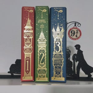 Può includere: Tre libri con copertina rigida di Harry Potter di J.K. Rowling, illustrati da MinaLima, con disegni in lamina d'oro su dorsi rossi, verdi e blu. I libri sono etichettati Año 1, Año 2 e Año 3, con una sagoma nera di un personaggio e un cartello 9 3/4.