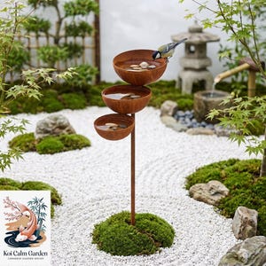 May include: A tiered bird bath featuring three stacked, rust-colored metal bowls supported by a single vertical pole. Each bowl contains water and small, smooth river stones. A small bird with yellow and black markings perches on the top bowl.