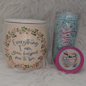 Puede incluir: Un juego de regalo con un tarro de cerámica beige con detalles florales y el texto "Everything I am, you helped me to be". Un tarro de ceras perfumadas azules con un logo de cebra y un recipiente rosa "Sea Salt & Vanilla."