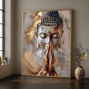 May include: A rectangular wall art print featuring a stylized Buddha with closed eyes and hands pressed together in a prayer position. The artwork uses a palette of metallic gold, silver, and grey tones with a textured, distressed paint effect.