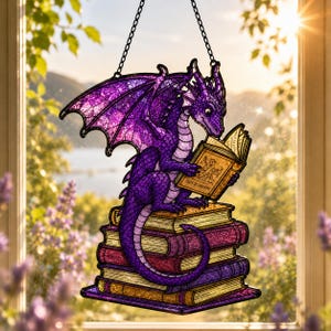 May include: A stained glass suncatcher featuring a purple dragon with textured wings perched atop a stack of four books. The dragon holds an open book with the text "TALES OF DRAGONS" clearly visible on the cover. The piece hangs from a black chain.