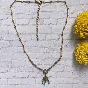 May include: A gold-toned necklace featuring a delicate chain with small turquoise beads, a lobster clasp, and an adjustable extender chain. The pendant consists of two stacked floral-shaped metal components with turquoise accents and a central stone.