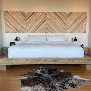 May include: A white bed with a wooden headboard and a cowhide rug on a wooden floor. The headboard is made of wood planks arranged in a chevron pattern.