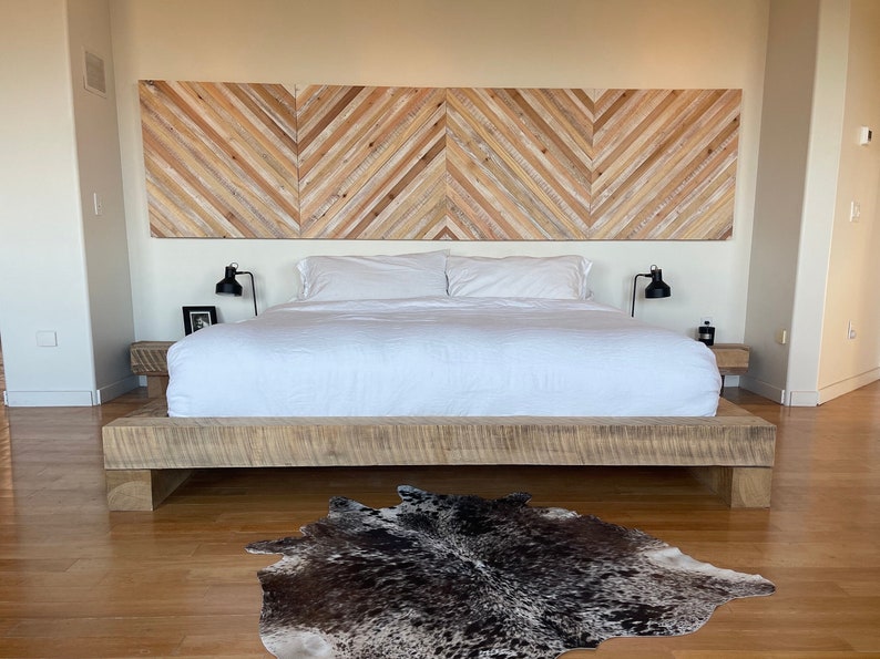 May include: A white bed with a wooden headboard and a cowhide rug on a wooden floor. The headboard is made of wood planks arranged in a chevron pattern.