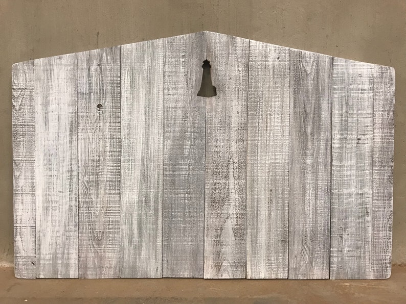 Puede incluir: Se&ntilde;al de madera blanqueada con un recorte de una campana en el centro. La se&ntilde;al est&aacute; hecha de madera recuperada y tiene un aspecto r&uacute;stico.