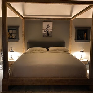 May include: A wooden canopy bed frame with a white duvet and pillows. The bed is in a bedroom with gray walls and a black and white photo on the wall.