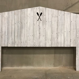 Puede incluir: Cabecero de madera blanqueada con un dise&ntilde;o sencillo y r&uacute;stico. El cabecero presenta un recorte de dos remos cruzados en el centro.
