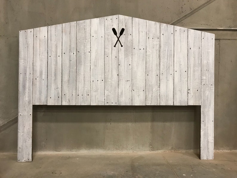 Puede incluir: Cabecero de madera blanqueada con un dise&ntilde;o sencillo y r&uacute;stico. El cabecero presenta un recorte de dos remos cruzados en el centro.