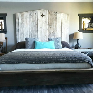 Puede incluir: Una cama king-size con una cabecera de madera y una manta de patr&oacute;n gris y blanco. La cabecera est&aacute; hecha de madera recuperada y tiene un dise&ntilde;o decorativo de flor de lis. La cama est&aacute; sobre una plataforma de madera.
