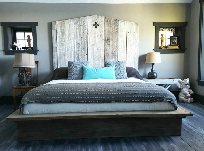 Puede incluir: Una cama king-size con una cabecera de madera y una manta de patr&oacute;n gris y blanco. La cabecera est&aacute; hecha de madera recuperada y tiene un dise&ntilde;o decorativo de flor de lis. La cama est&aacute; sobre una plataforma de madera.