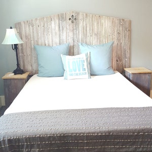 Puede incluir: Una cama blanca con una cabecera de madera y una almohada a rayas azules y blancas con el texto "Love and the Beach". La cama tiene una manta a rayas grises y blancas y est&aacute; sobre un suelo de madera.