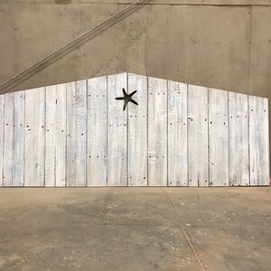 Puede incluir: Estructura de madera blanqueada que se asemeja a un granero con un recorte en forma de estrella de mar en el centro. La estructura est&aacute; de pie sobre un suelo de hormig&oacute;n.