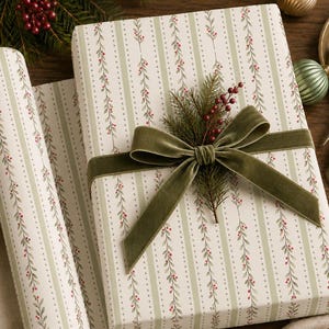 May include: A rectangular gift wrapped in white paper with a pattern of vertical green stripes, dotted lines, and trailing vines with small red berries. The package is tied with a wide olive green velvet ribbon and topped with a sprig of pine.