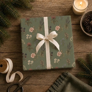 Pu&ograve; includere: Una scatola regalo quadrata avvolta in carta verde salvia con una stampa botanica di rose rosa, margherite bianche, rametti di lavanda e bacche scure. Il pacchetto &egrave; legato con un nastro di tessuto color crema in un semplice fiocco.