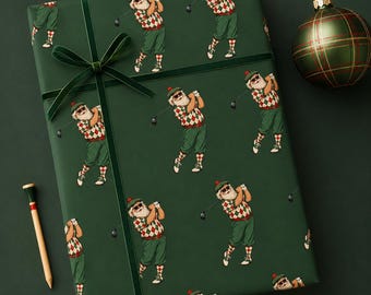 Pode incluir: Papel de embrulho verde-escuro com um padrão repetitivo de Pais Natal a jogar golfe, usando óculos de sol, bonés e camisolas de losangos. O papel está atado com uma fita de veludo verde-escura e acompanhado por um tee de golfe de madeira.