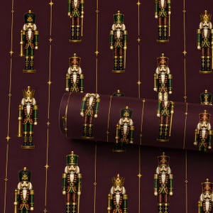 Pode incluir: Papel de presente com um padr&atilde;o repetitivo de figuras de quebra-nozes em uniformes verdes, vermelhos e dourados sobre um fundo bord&ocirc; profundo. O design inclui linhas verticais douradas finas e pequenos detalhes de estrelas douradas.