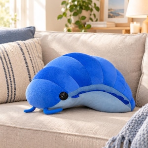 Op de afbeelding: Een pluche speelgoed in de vorm van een pissebed in blauwtinten. Het wezen heeft een afgeronde, gesegmenteerde rug in levendig blauw, een lichtblauwe onderkant, twee kleine voelsprieten aan de voorzijde en een groot, donker, glanzend oog.