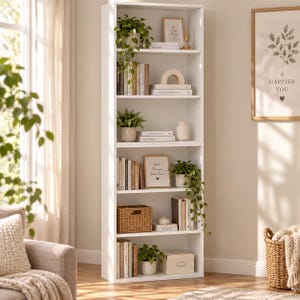 May include: A tall white bookcase with five shelves, filled with various books, potted green plants, a woven basket, a white storage box, and decorative items. The shelves are organised with books standing vertically and horizontally, interspersed with greenery.