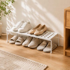 Pode incluir: Uma sapateira de metal branco com uma superfície de grade retangular e quatro pernas. O suporte contém dois tênis brancos, duas sapatilhas bege, dois tênis bege e dois chinelos bege dispostos em duas fileiras na superfície da prateleira.