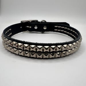 May include: Black leather dog collar with two rows of silver pyramid studs. The collar has a metal buckle and a D-ring for leash attachment. A punk rock style accessory.