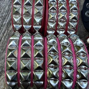 Puede incluir: Cuatro bandas de cuero con tachuelas plateadas y costuras rosas. Las bandas est&aacute;n apiladas una encima de la otra.