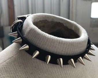 Op de afbeelding: Een zwarte leren choker met zilveren piramidevormige studs. De choker is op een witte stoffen mannequin.