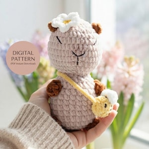 May include: A light beige crocheted animal figure with dark brown ears and paws, wearing a white flower on its head and a yellow crossbody bag. The text on the image reads DIGITAL PATTERN (PDF Instant Download).
