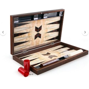 May include: A wooden backgammon board set featuring a dark brown frame with a light burl wood interior inlay. The board includes alternating dark and light triangular points, two red plastic dice cups, two white dice, and a set of white game checkers.