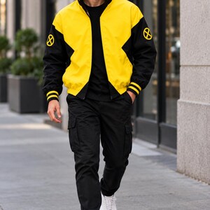 Man walking on a city street wearing yellow and black bomber jacket with black pants, casual streetwear outfit