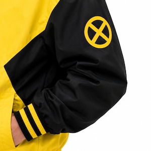 Close-up of black sleeve with yellow X logo patch and yellow striped ribbed cuff on men's bomber jacket