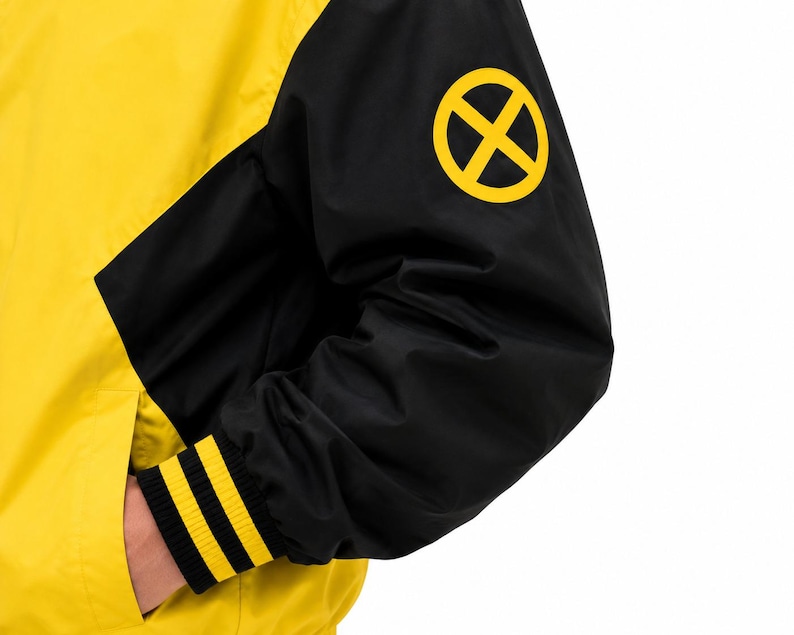 Close-up of black sleeve with yellow X logo patch and yellow striped ribbed cuff on men's bomber jacket