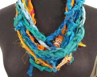 May include: A colorful fabric necklace with turquoise, blue, and yellow strands. The necklace is made of recycled saris and is a unique and stylish accessory.